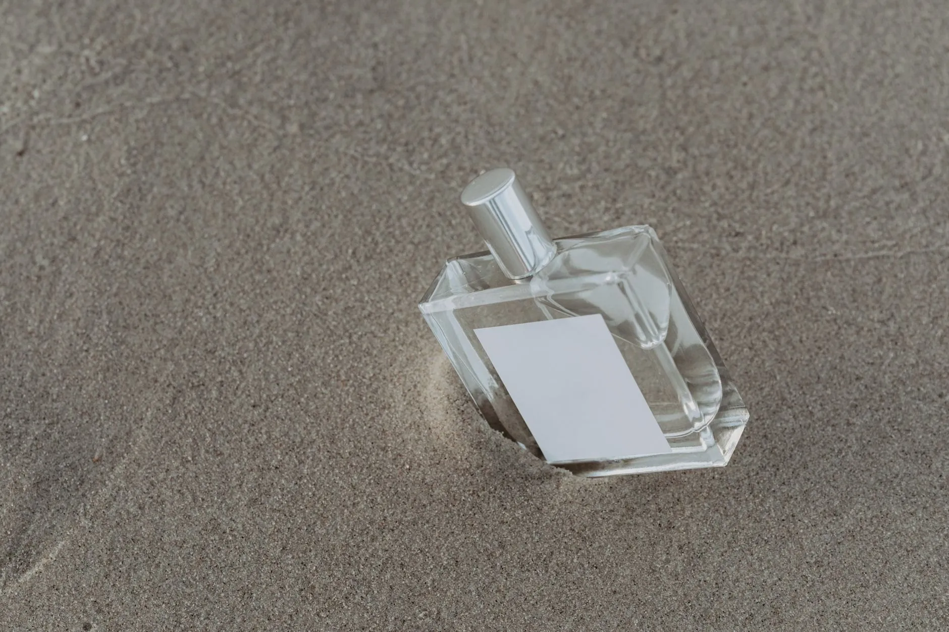 A clear, square Orrishaw bottle with a blank label lying in smooth grey sand