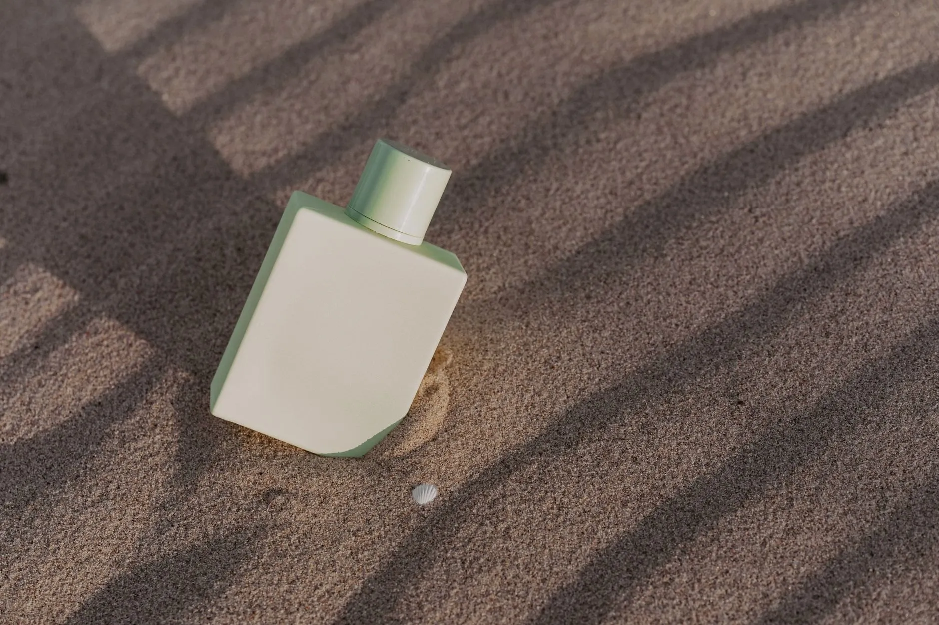 A frosted cream Orrishaw bottle lying in sand under hard stripes of shadow