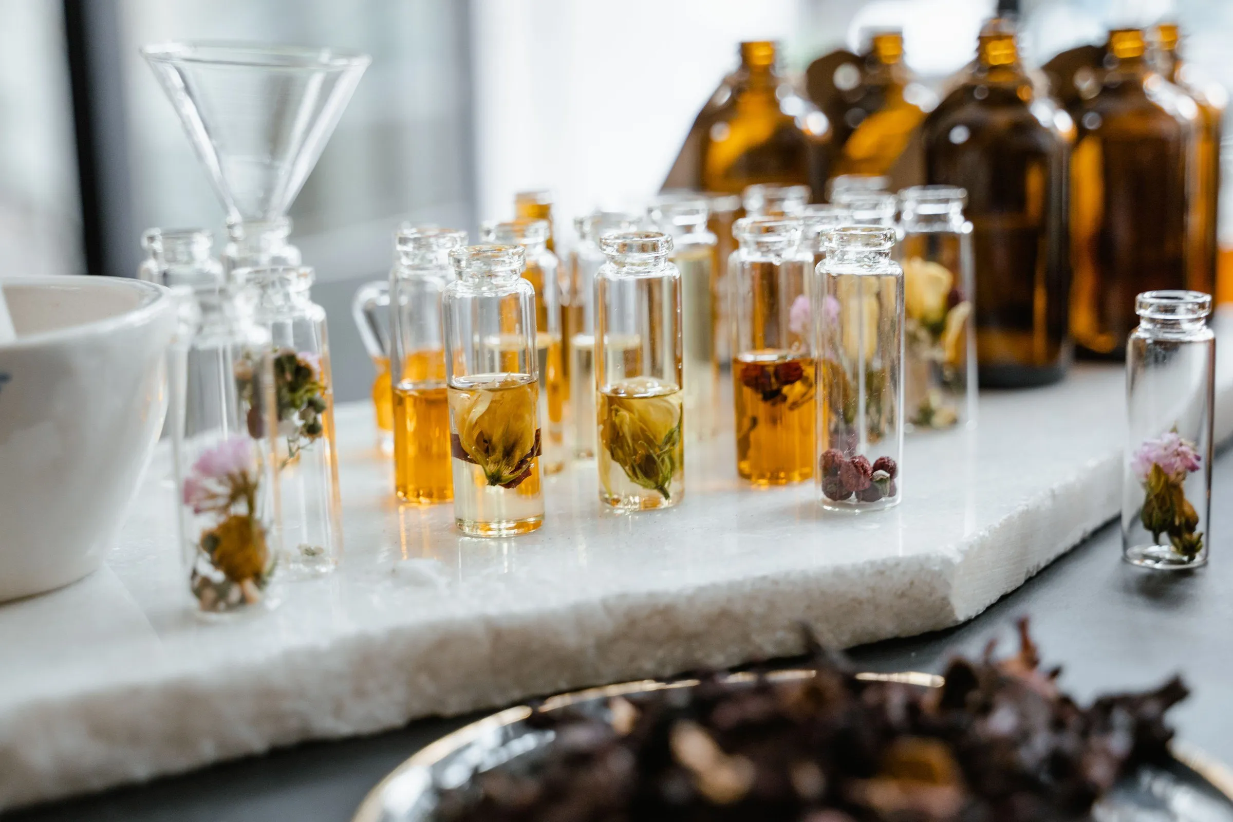 Small glass vials of fragrance and amber bottles on a white marble slab in the perfumer's workshop